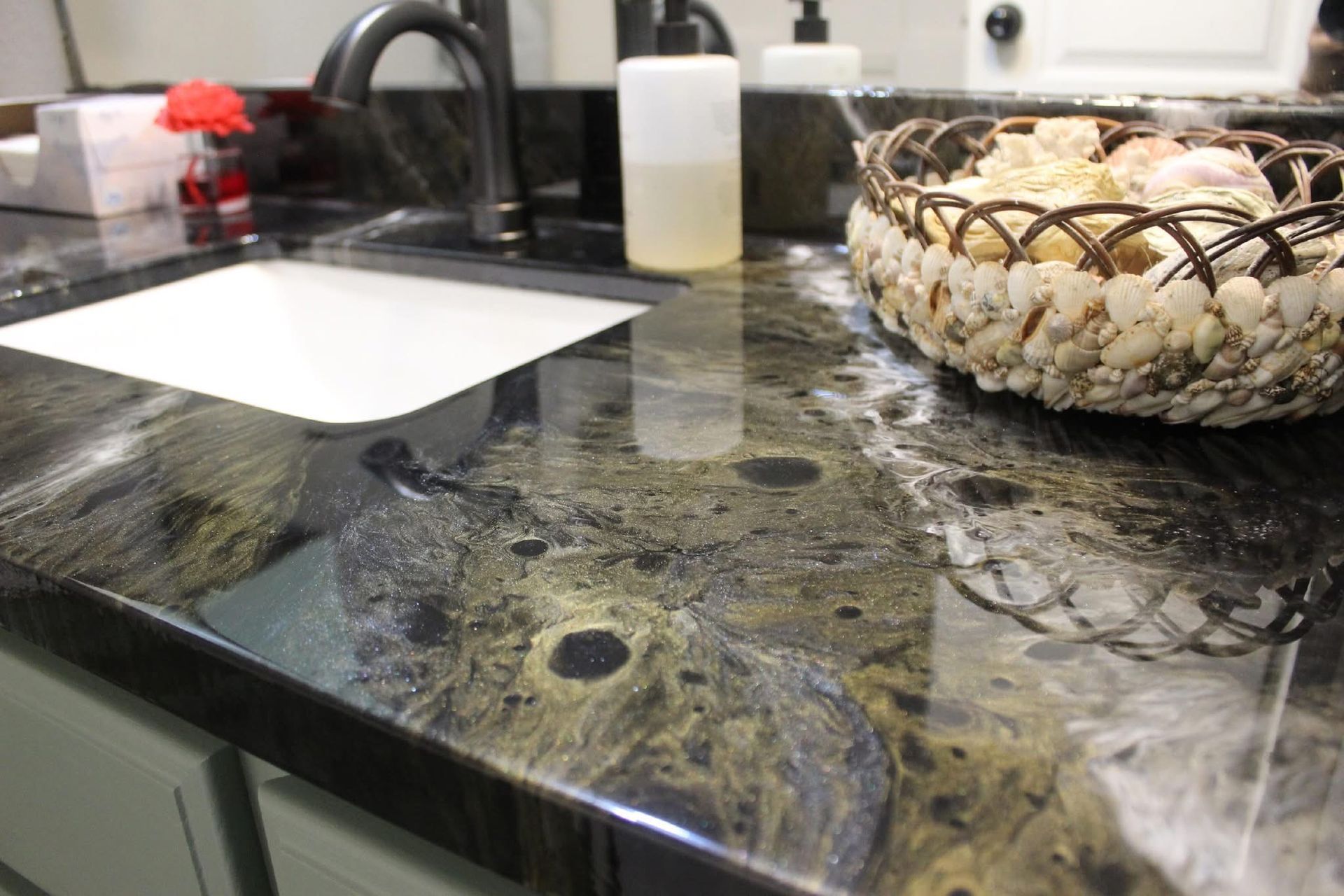 Kitchen countertop with sink, soap dispenser, and decorative bowl on a dark marble surface.