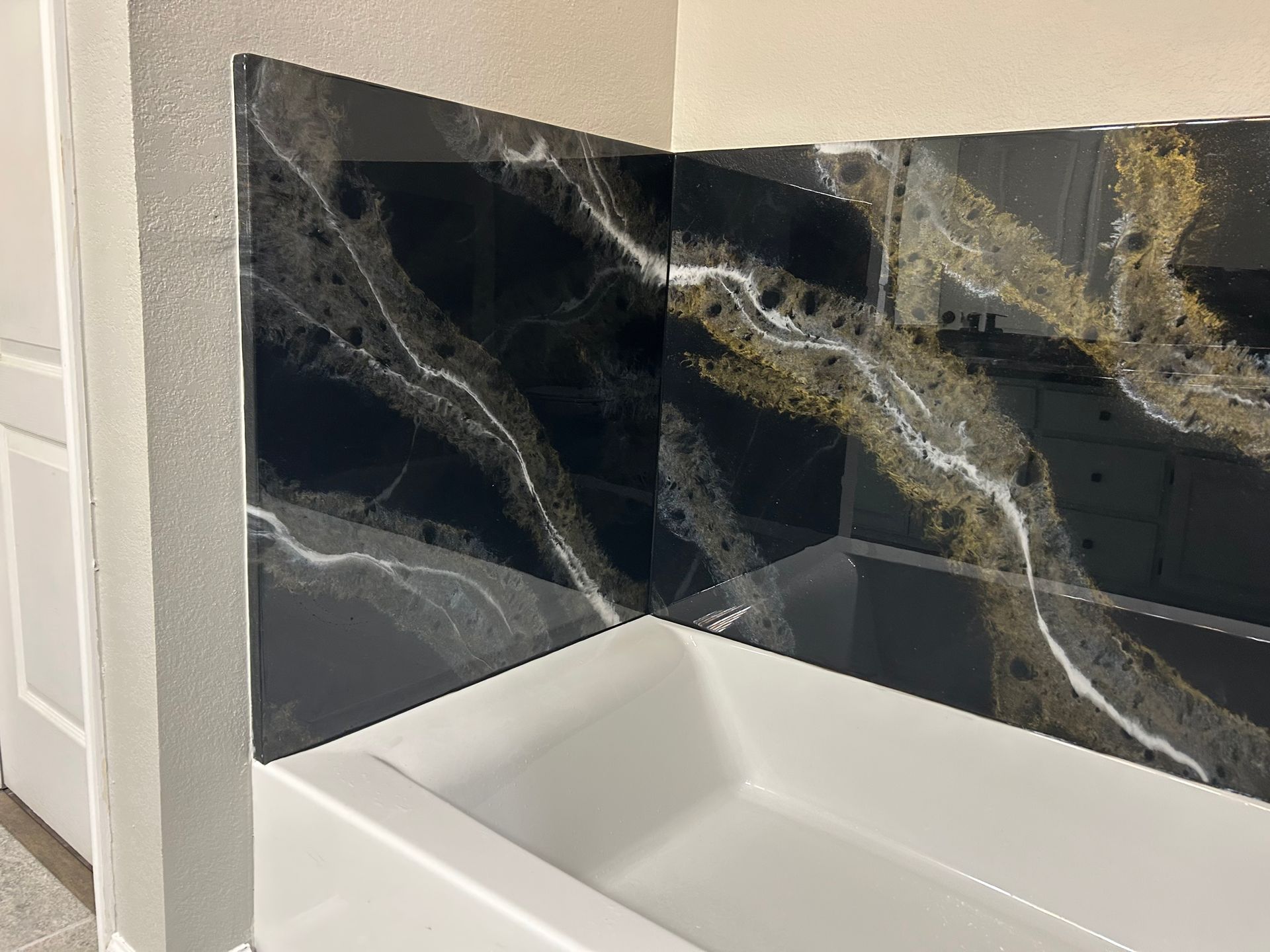 White bathtub corner with glossy black marble tile and gold veining in a bathroom.