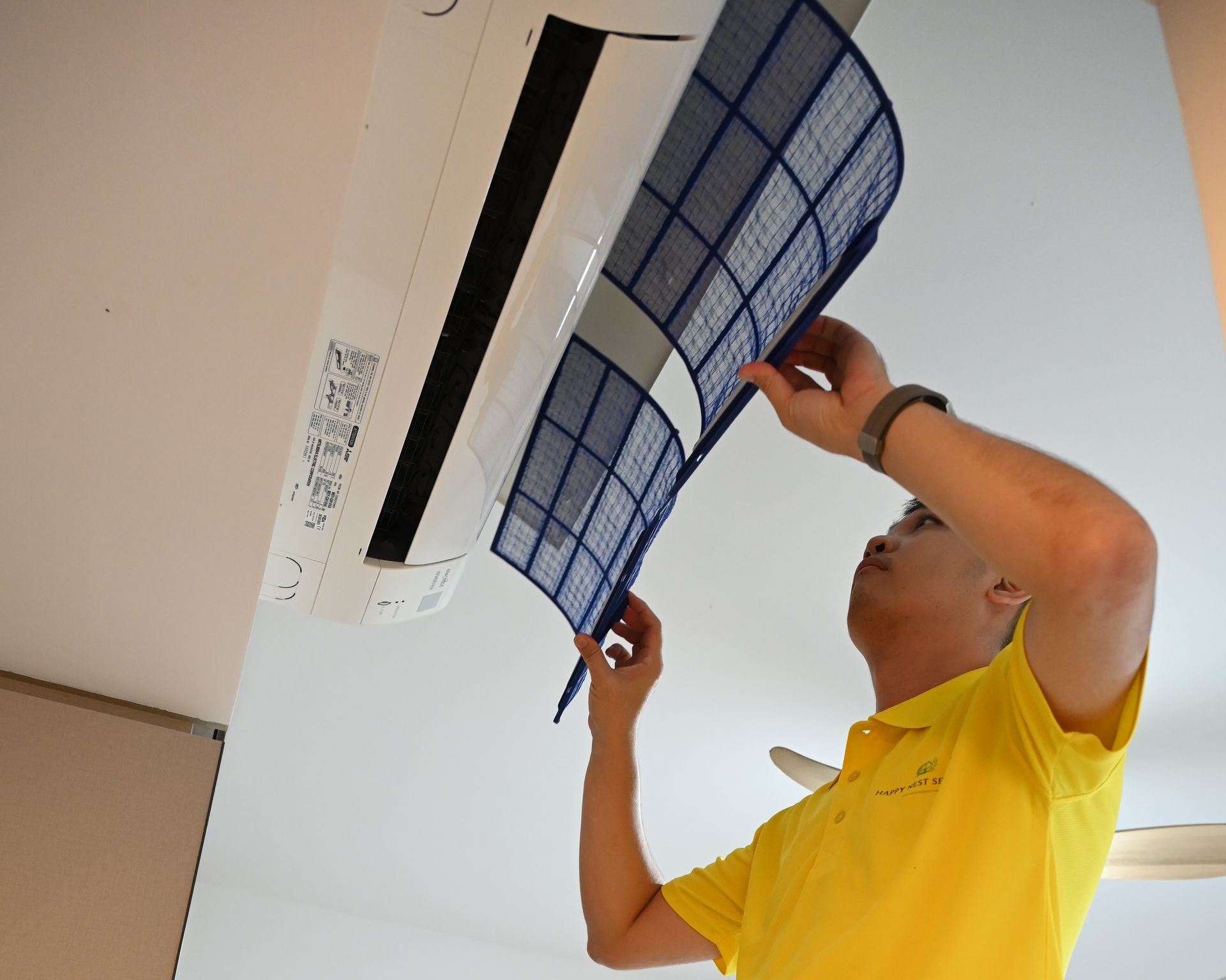 Man in yellow shirt removes air filter from air conditioner.