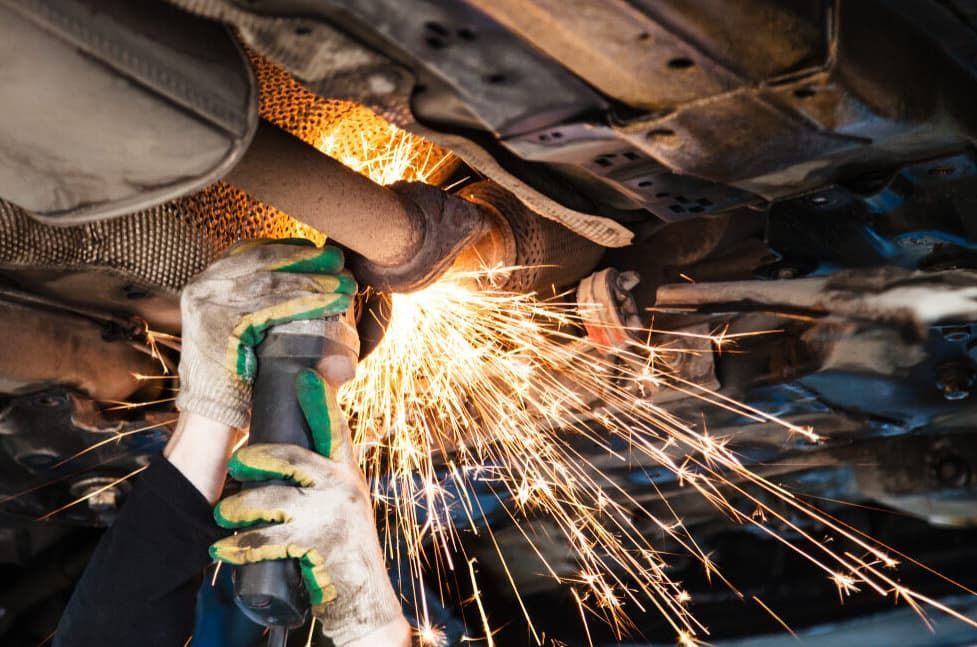 A Mechanic Cuts An Exhaust Pipe Under A Car — Darwin Auto Mobile Care in Woolner, NT