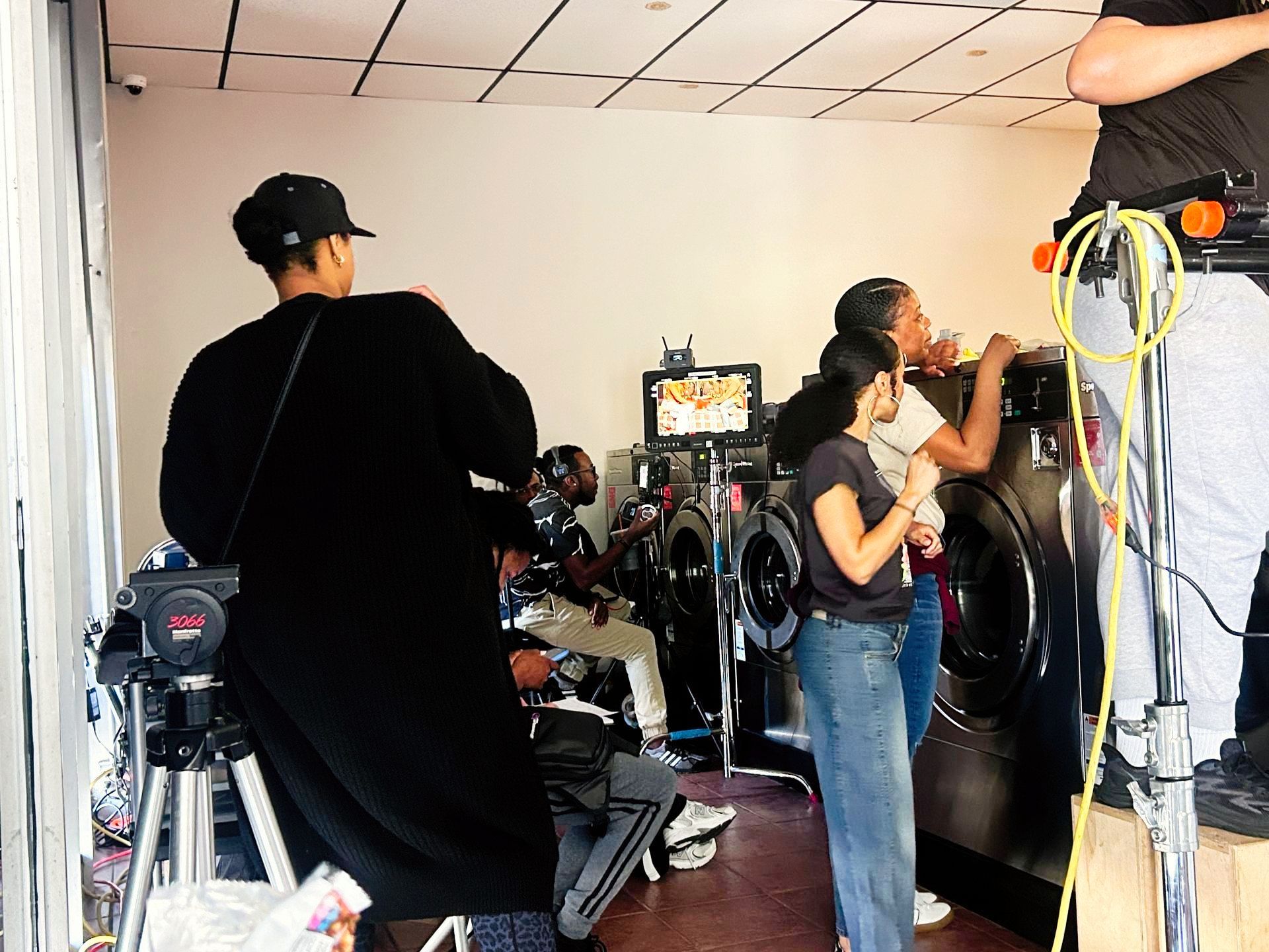 People filming a video shoot in a studio, with cameras, lights, and a makeup station.