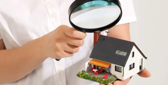 A person is holding a magnifying glass over a model house.