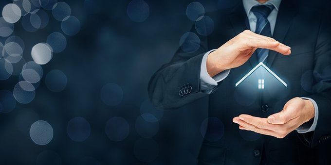 A man in a suit and tie is holding a house in his hands.