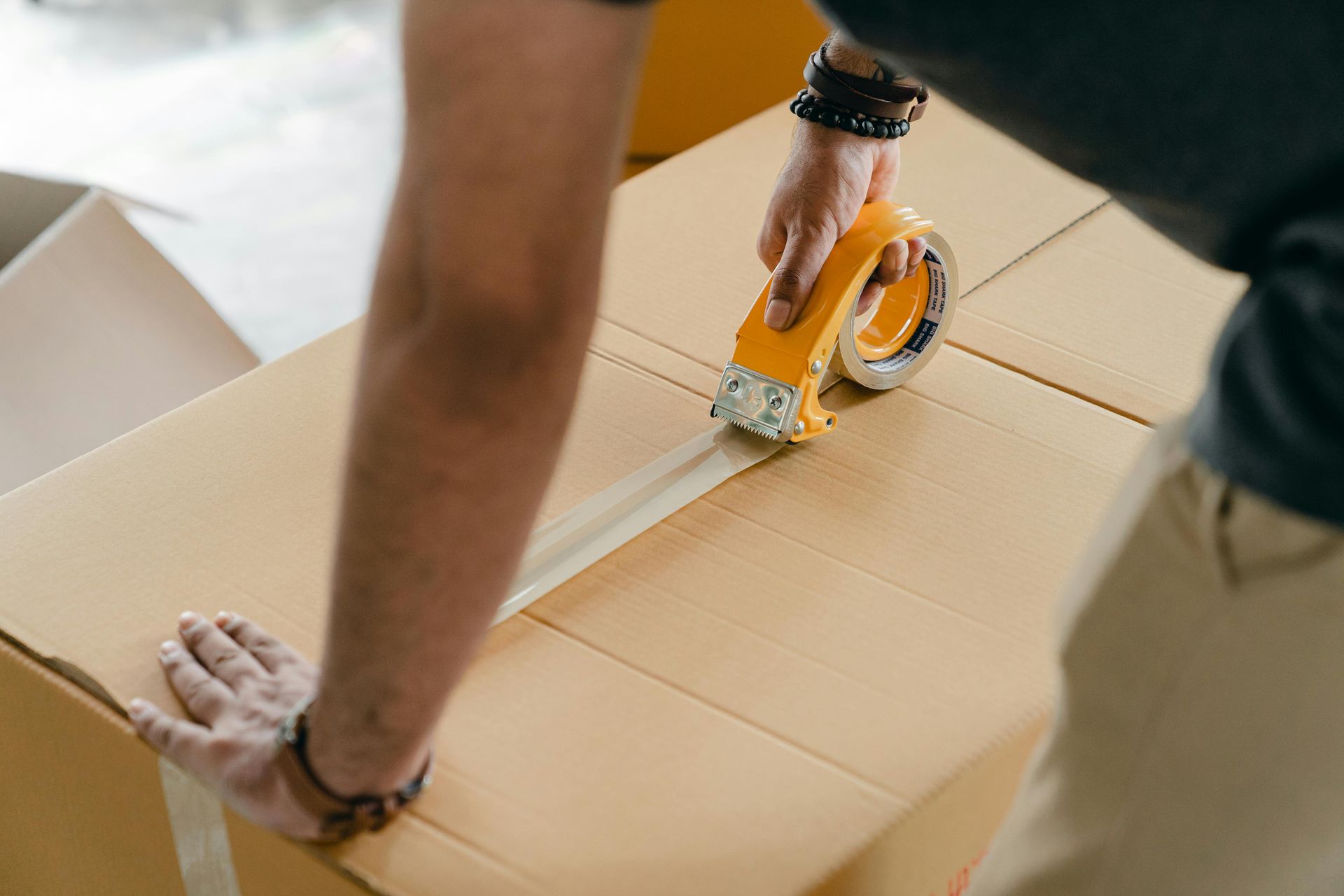 Person sealing a cardboard box with packing tape, preparing for a move.