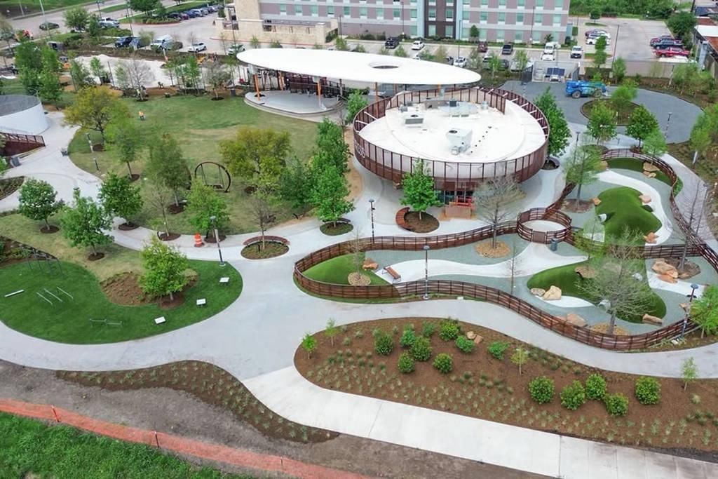 Aerial view of a landscaped park with winding paths, trees, and round pavilion-like buildings