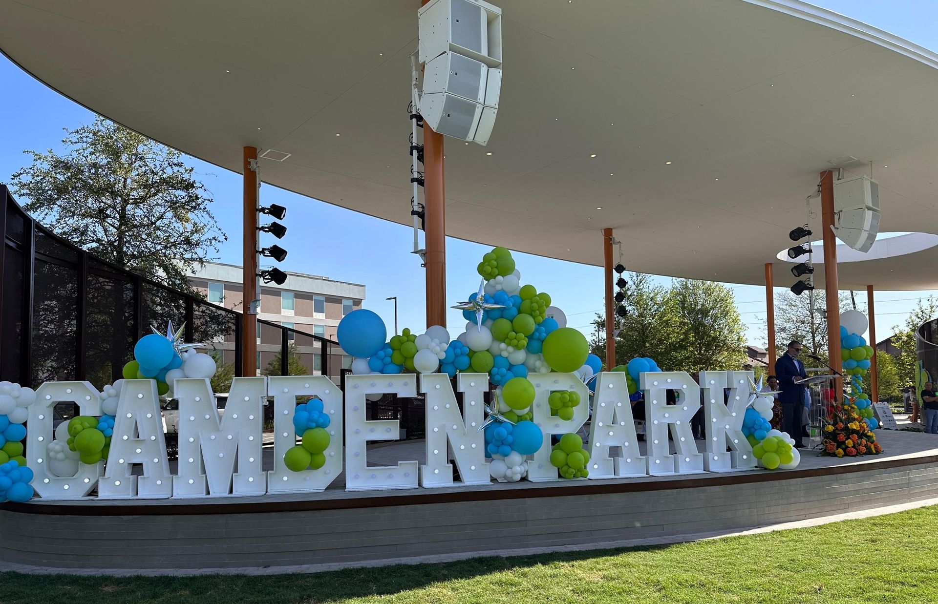 CAMDEN PARK sign with blue and white balloons under a pavilion on a sunny day