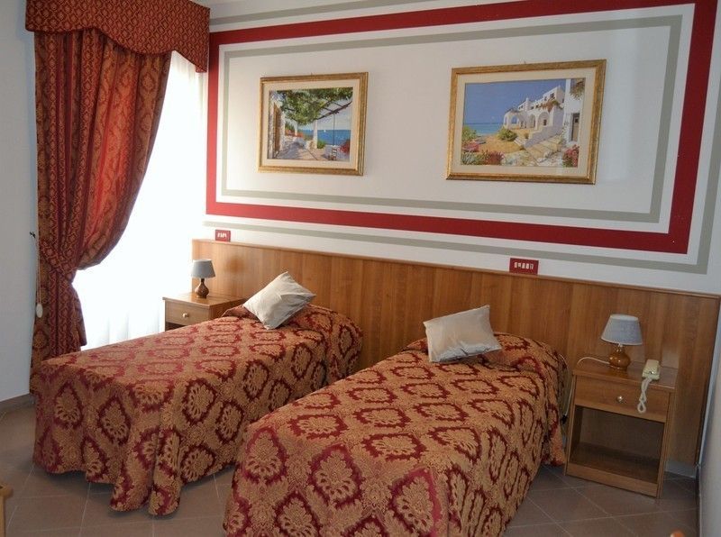Due letti singoli in una camera d'albergo con biancheria da letto con motivi rossi e dorati e opere d'arte.