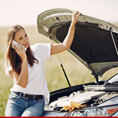 Mulher com problemas no carro ao telefone, capô aberto, ao ar livre, campo ao fundo.