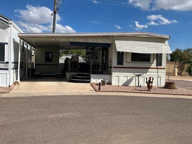 Mobile home with carport, front porch, and small landscaped yard under cloudy skies