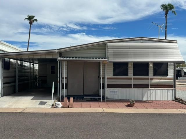 Single-wide mobile home with carport and palm trees in a sunny desert park