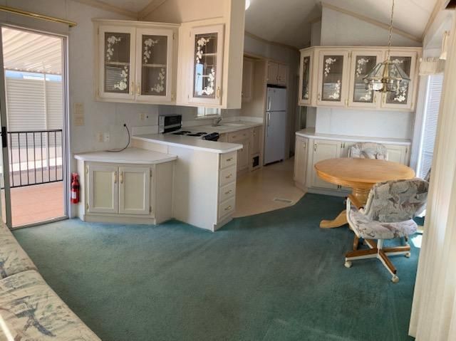 Empty kitchen and dining area with white cabinets, teal carpet, and sliding glass door to a balcony.
