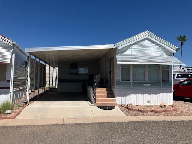 Single-wide mobile home with carport and palm trees in a sunny desert park