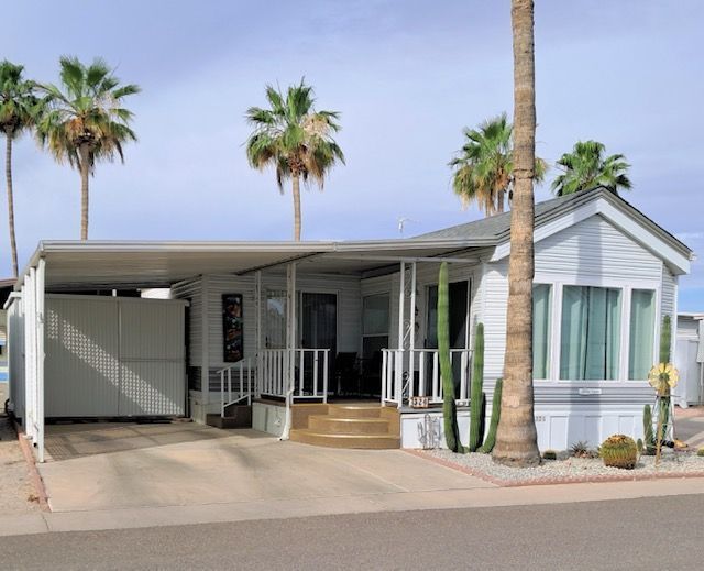 White mobile home with carport and palm trees in a sunny residential park