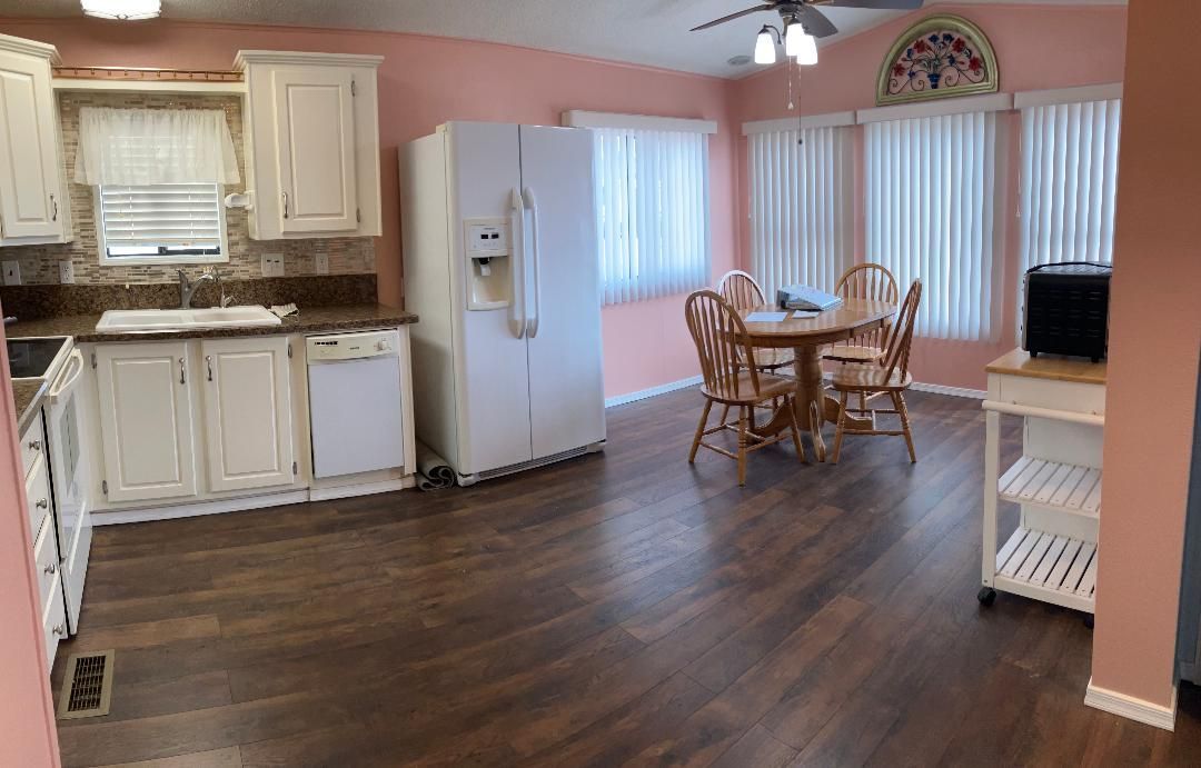 Kitchen and dining area with white cabinets, fridge, wooden floor, and a table by sliding glass doors.
