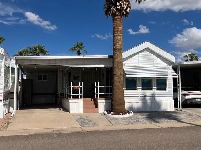 Single-wide mobile home with carport and palm trees in a sunny desert park