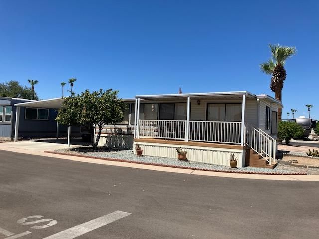 Single-wide mobile home with carport and palm trees in a sunny desert park