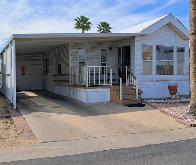 White manufactured home with a front porch, carport, and desert landscaping by the street