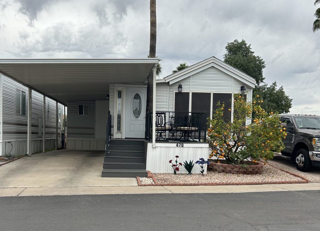 Mobile home with carport, front porch, and small landscaped yard under cloudy skies