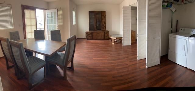Open living and dining room with hardwood floors, dark table and chairs, brick fireplace, and white kitchen appliances