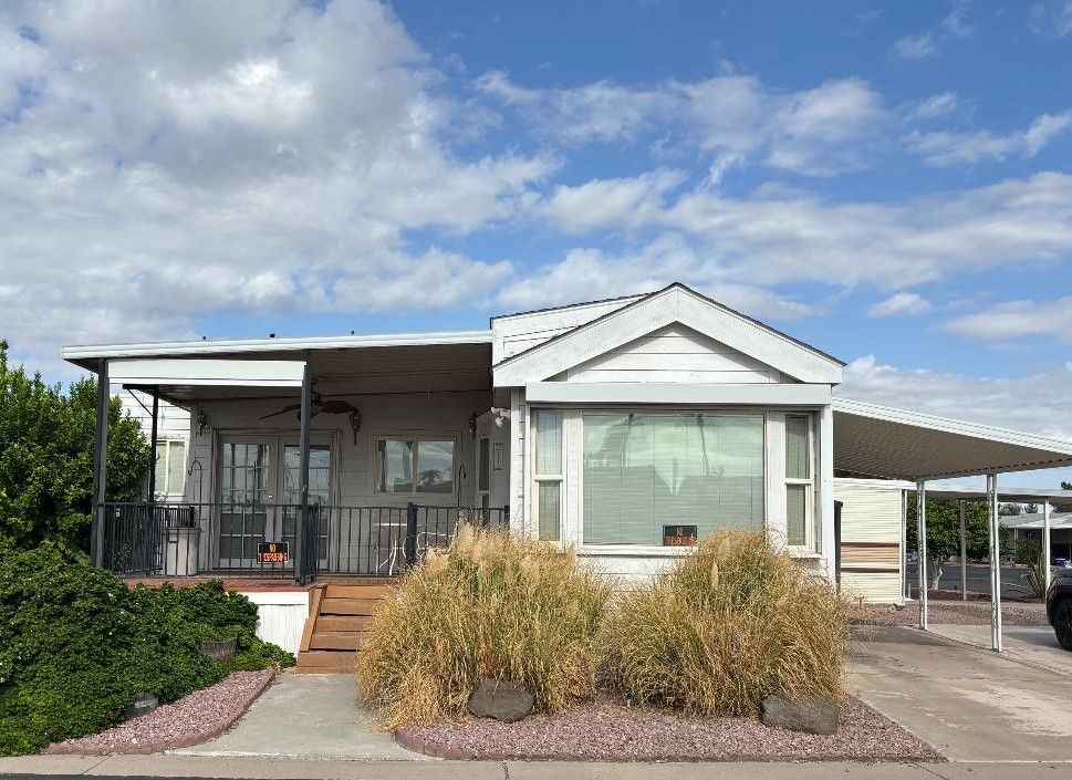 Single-wide mobile home with carport and palm trees in a sunny desert park