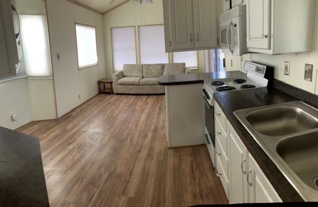 Bright kitchen and living area with white cabinets, wood floors, black countertop, sink, and beige sofa.