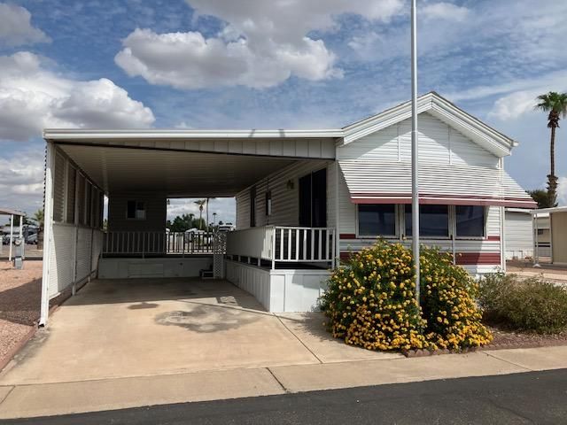 Single-wide mobile home with carport and palm trees in a sunny desert park