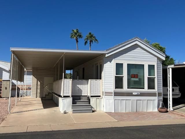 Single-wide mobile home with carport and palm trees in a sunny desert park