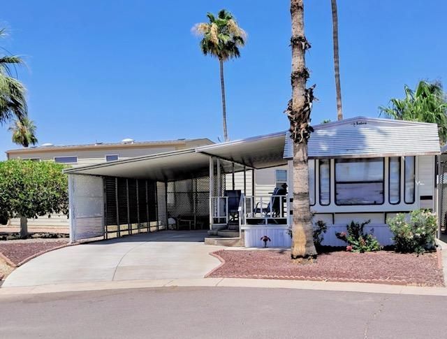 Desert home with carport, white trailer, and palm trees along a quiet street