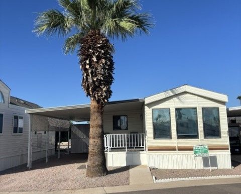 Mobile home with a carport and a palm tree in front, on a quiet residential street.