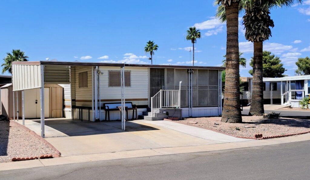 Single-wide mobile home with carport and palm trees in a sunny desert park