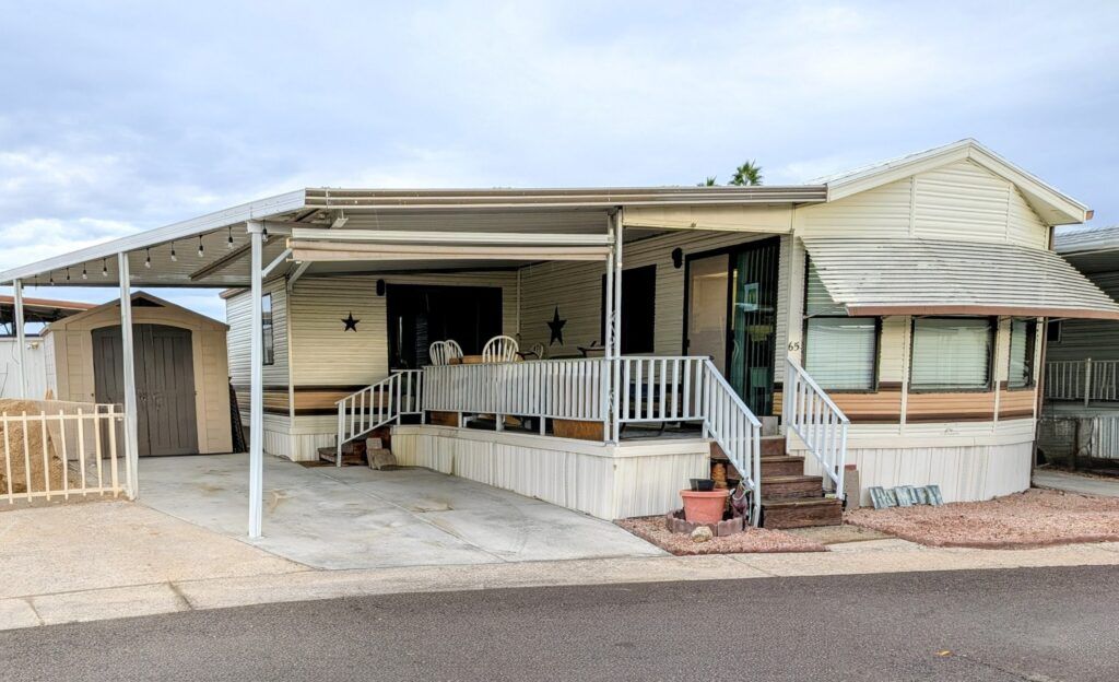 Single-story beige mobile home with a covered porch, ramp, and driveway in a desert setting.
