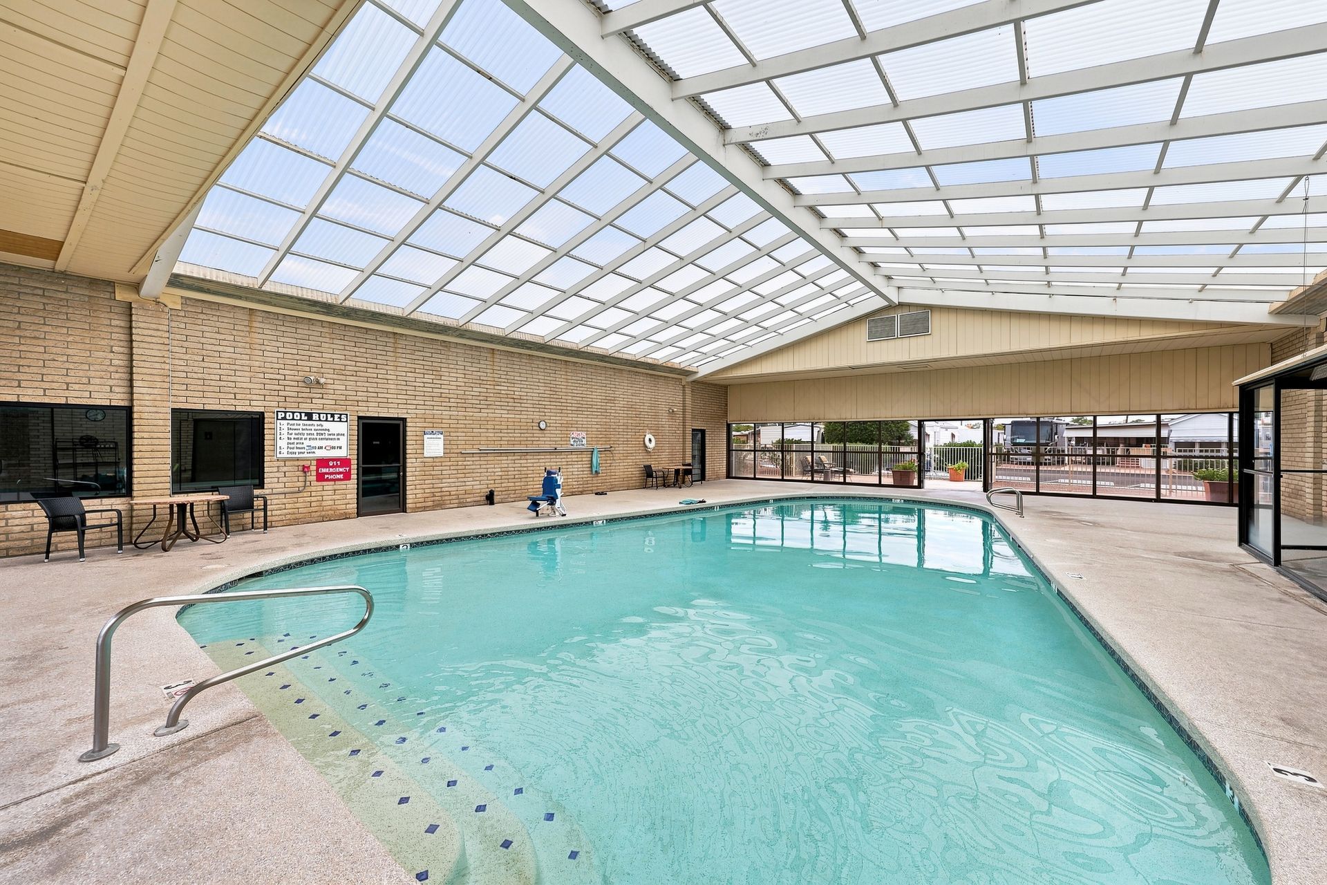 Indoor pool with sunlit water, lounge chairs, and a high glass ceiling.