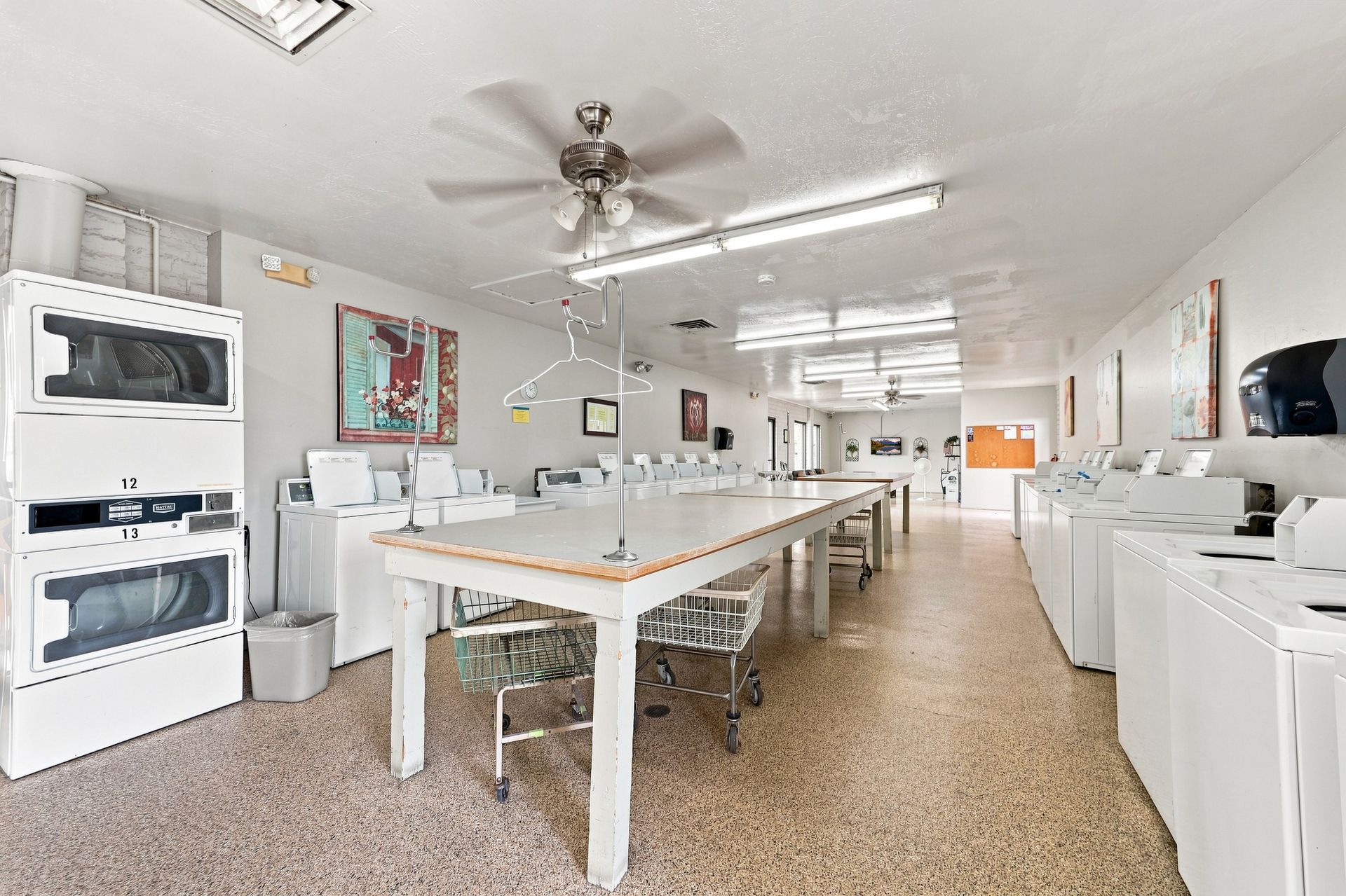 Bright laundry room with rows of white washers and dryers and a central folding table
