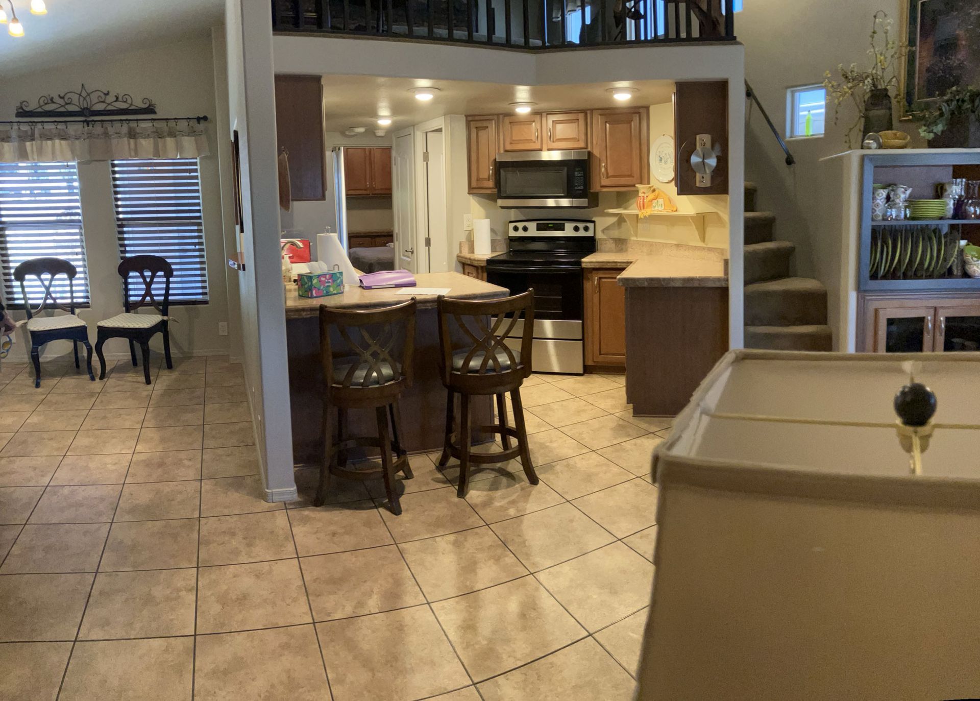 Open kitchen and dining area with tiled floor, island stools, and beige couches under warm lighting