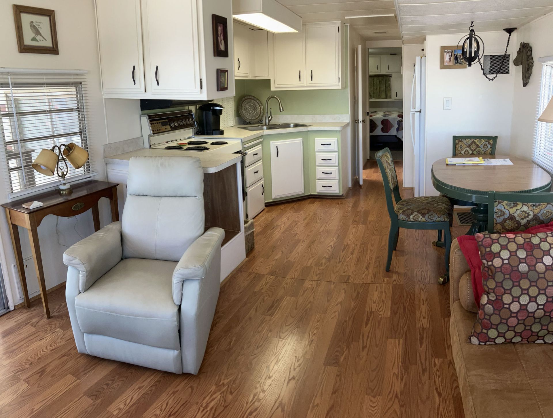 Bright kitchen and dining area with white cabinets, wood floors, recliner, and round table near a doorway