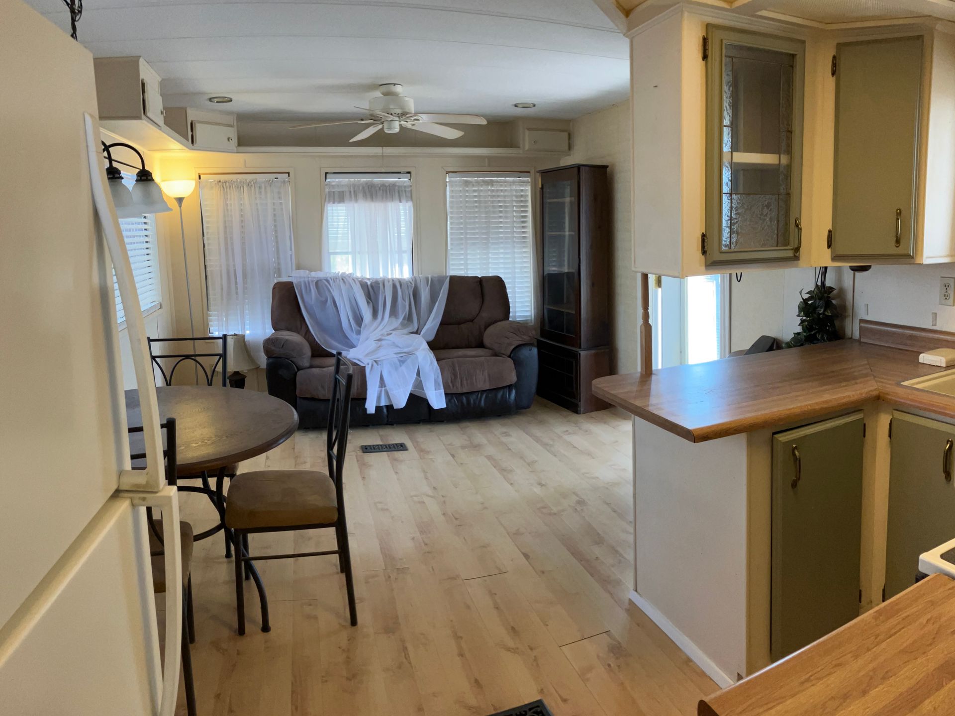 Living room and kitchen view with brown couch, chair, and light wood floors