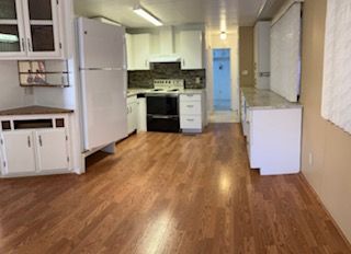Empty kitchen with wood floors, white cabinets, stove, refrigerator, and a doorway at the back.