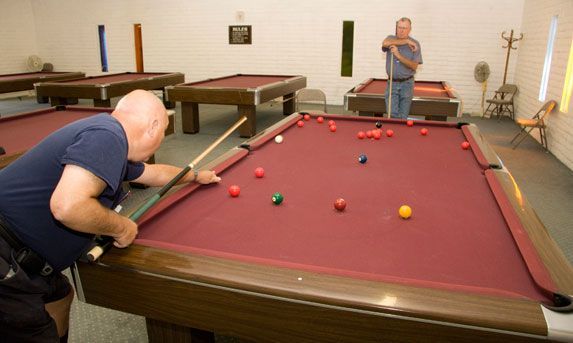 Man aiming a shot at a billiards table in a game room, with another person standing nearby.