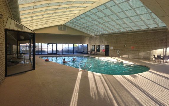 Indoor swimming pool with turquoise water, skylights, and sunlit shadows on the deck