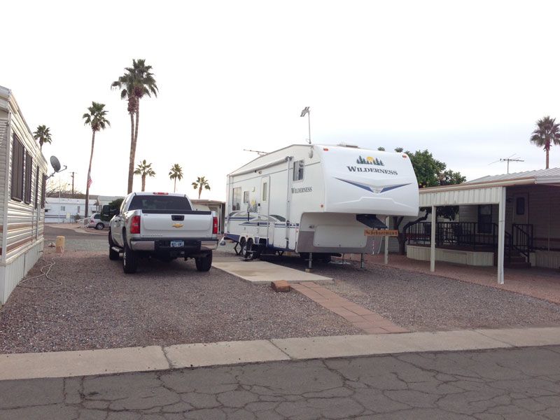 Pickup truck and white RV parked in a desert campground with palm trees and covered sites.
