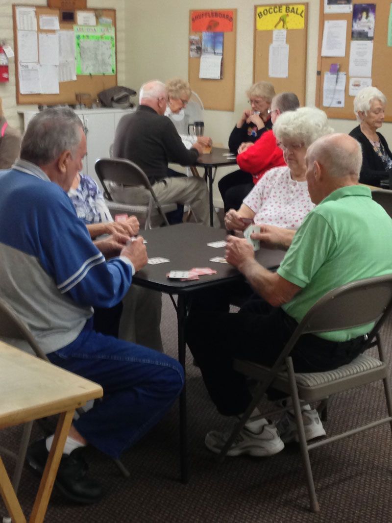 People seated around tables in a community room, playing cards and chatting.