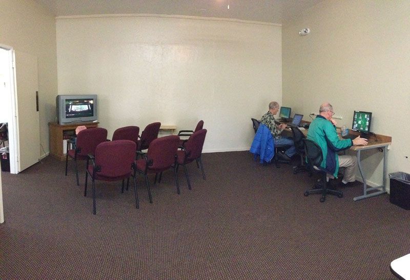 Small meeting room with chairs facing a TV and two people working at a computer table