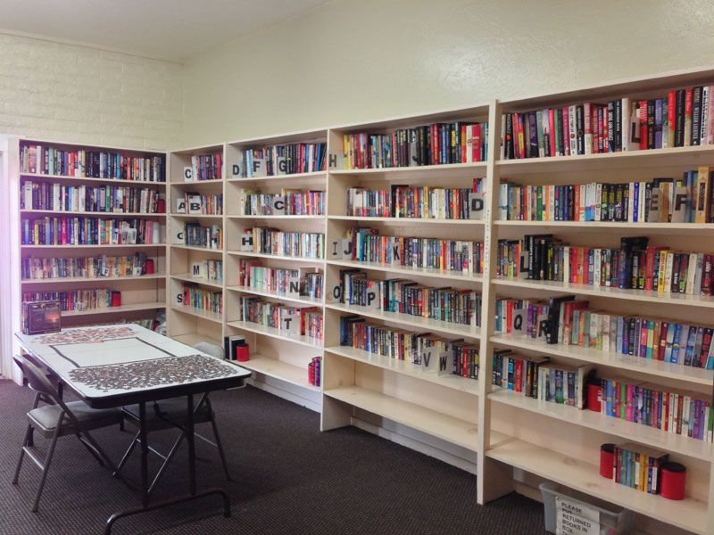 Bright library room with white bookshelves filled with books and a table in the foreground.