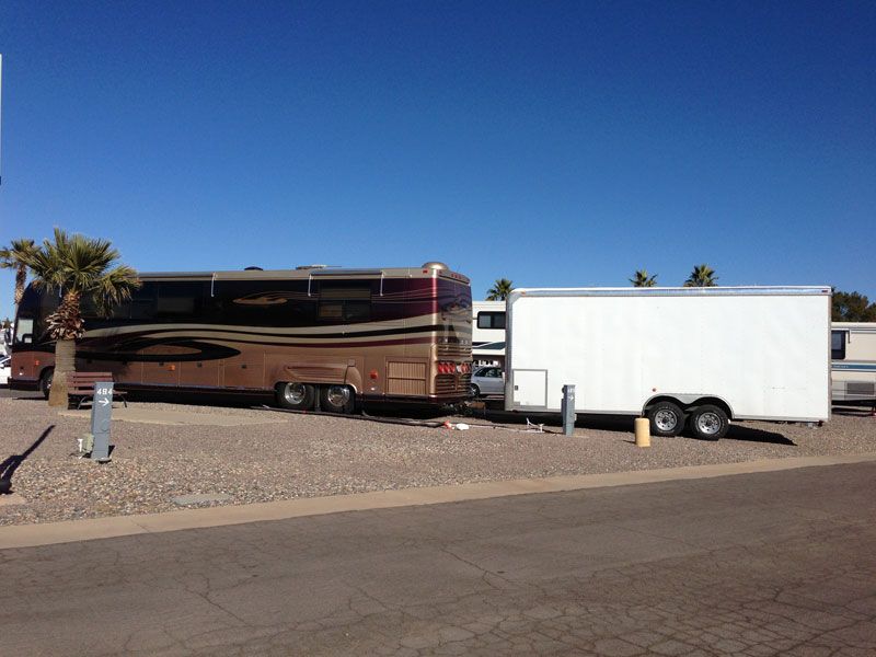 Two parked RVs with a white trailer on a desert roadside under a clear blue sky.