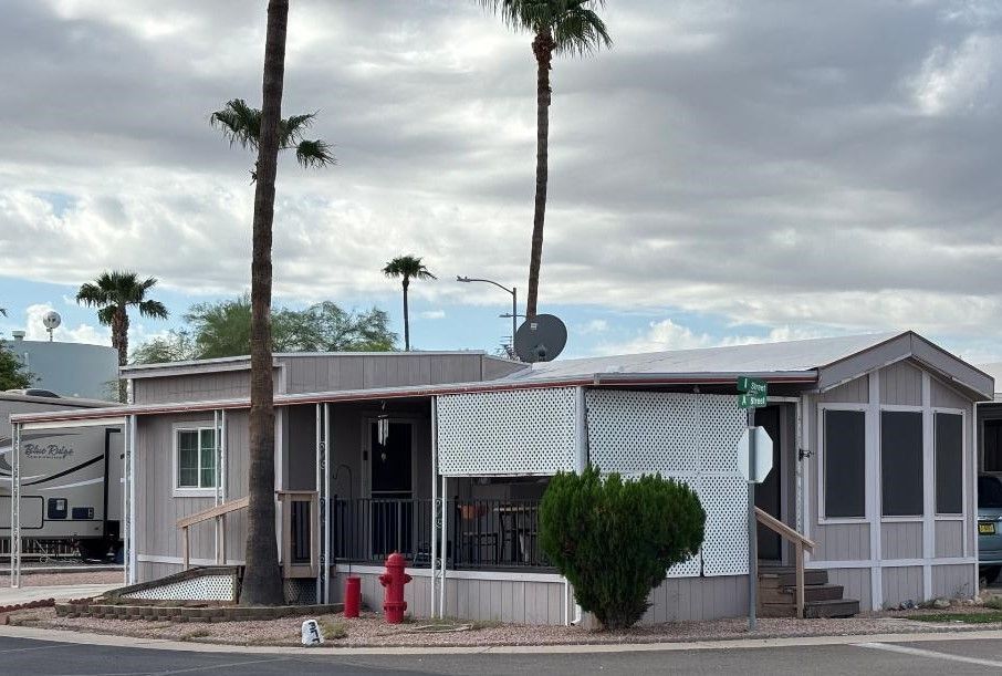 White manufactured home with porch and blue canopy beside a concrete driveway under a cloudy sky
