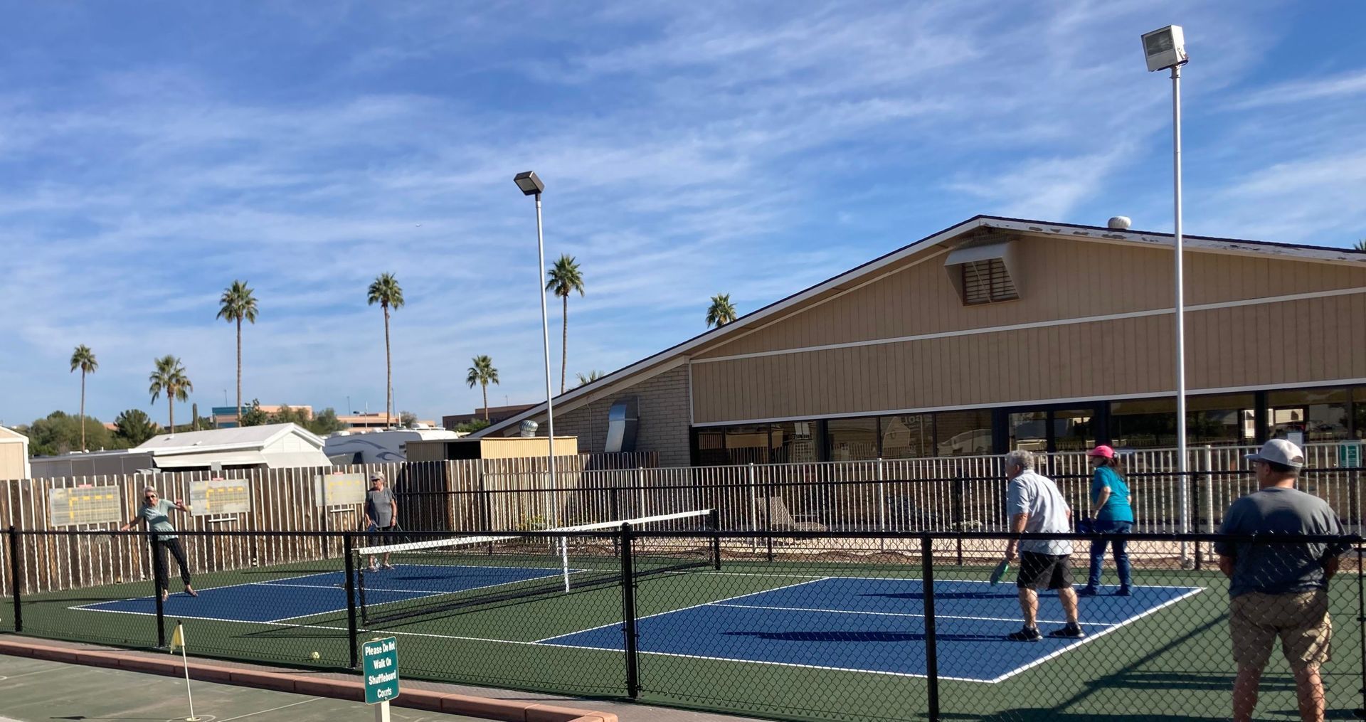 Outdoor mini-golf course with green lanes, wooden fences, and two people near the far end under a sunny sky