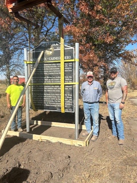 Three men installing historical marker about Santa Fe Trail; field setting, sunny day.