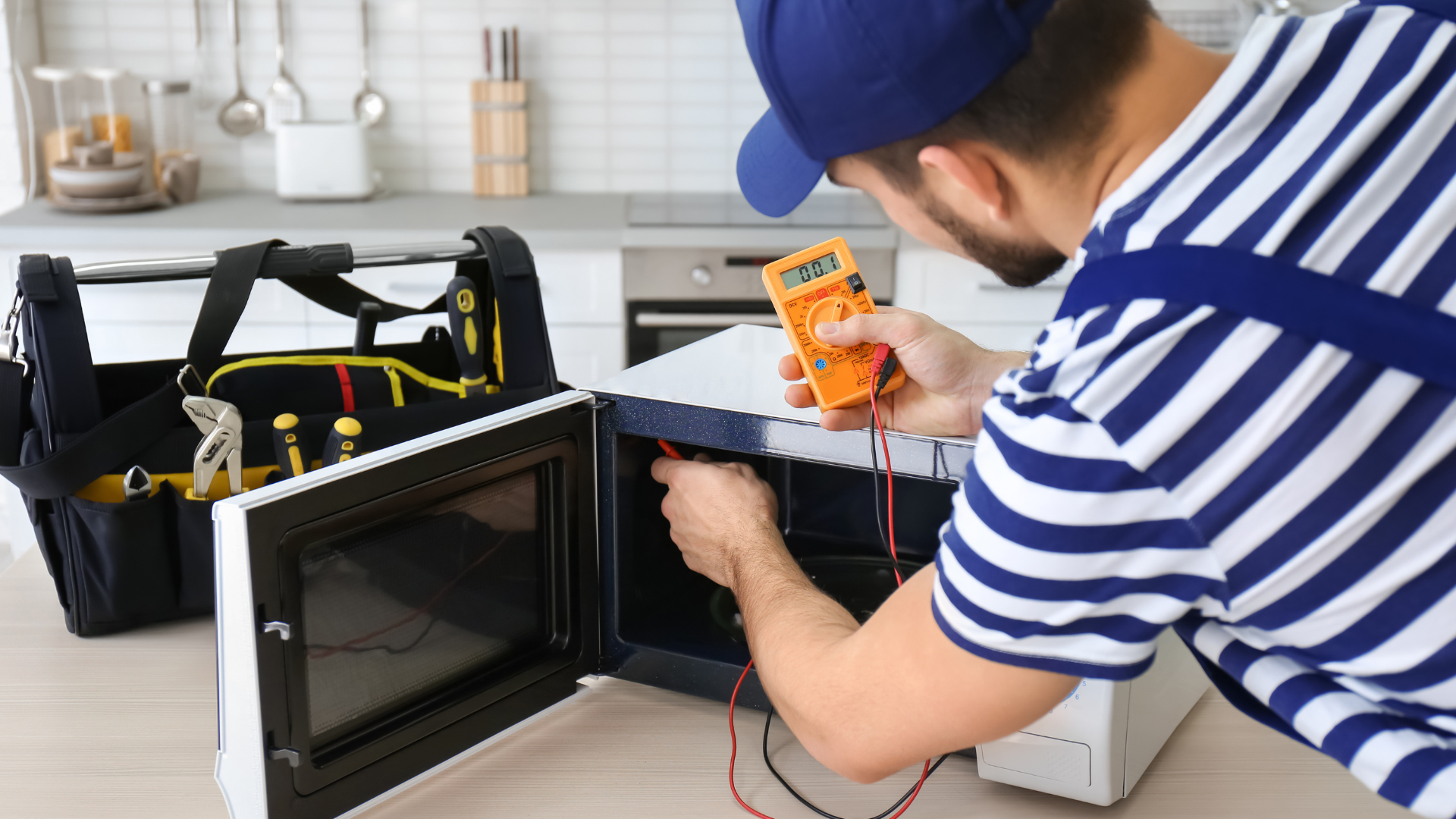 A man is fixing a microwave oven in a kitchen.