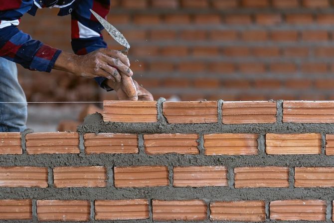 Hands placing wet mortar on a brick wall under construction