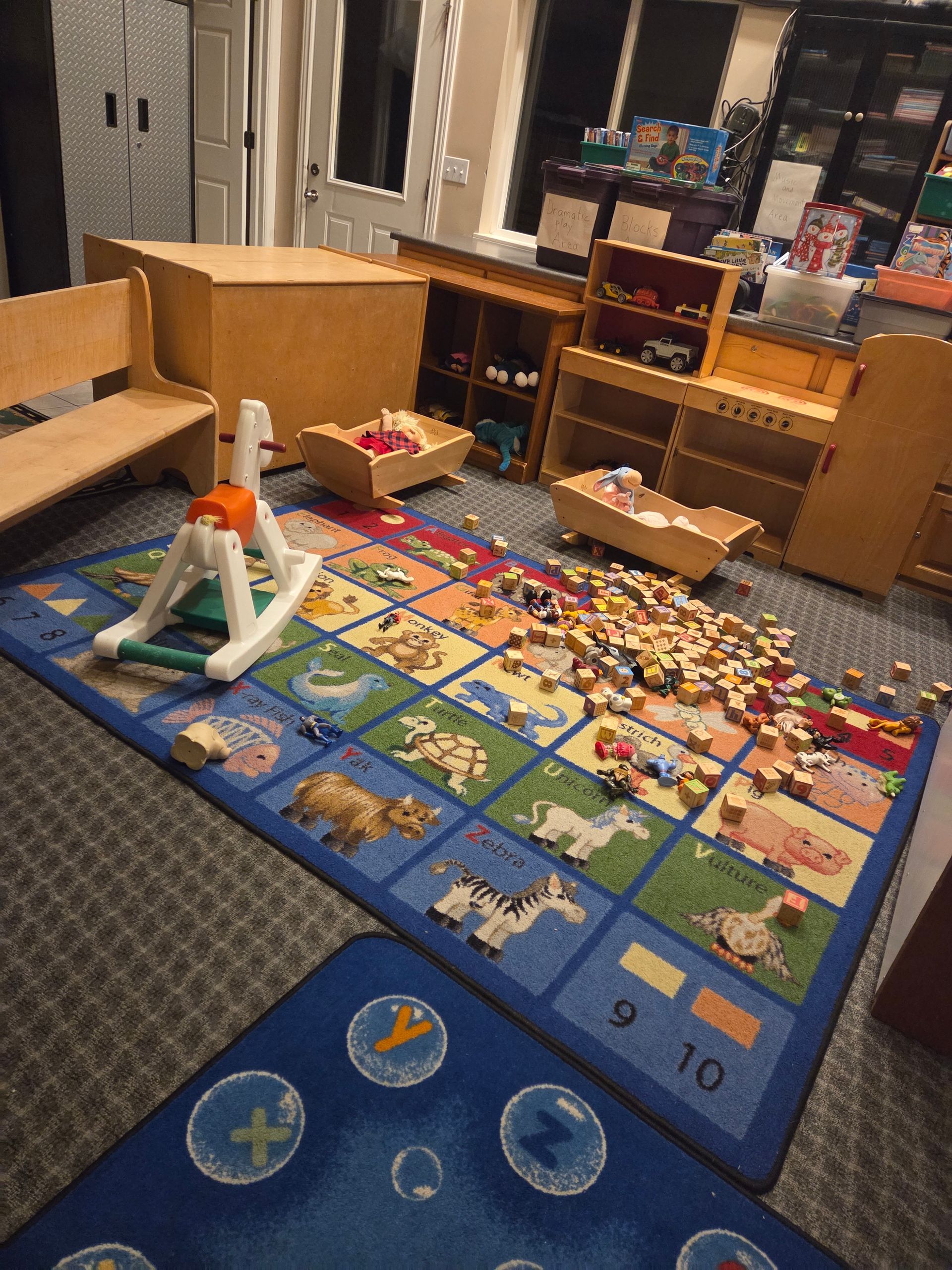 Children’s playroom with a colorful alphabet rug, scattered toys, and wooden storage furniture.